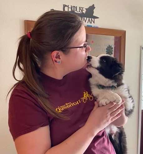 Image is of a black and white puppy kissing the face of the author, Megan.
